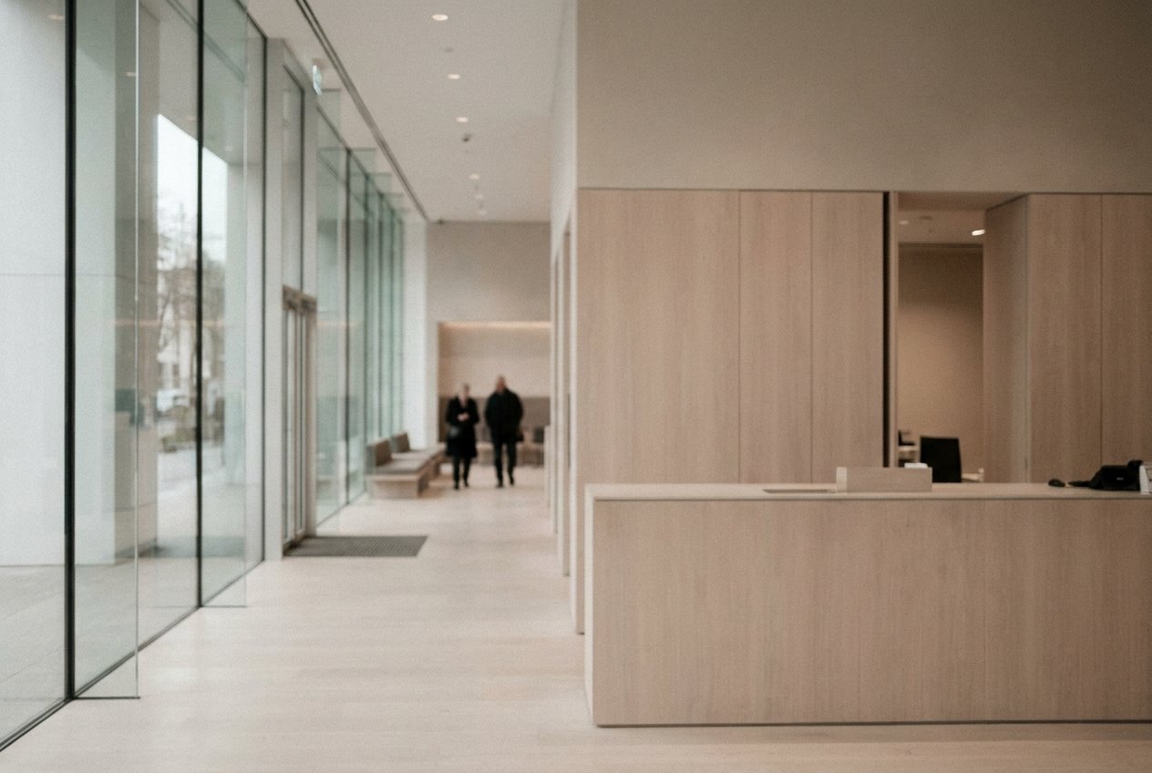 The quiet interior of a modern bank branch, pale joinery and a low counter, daylight through a full-height glass frontage